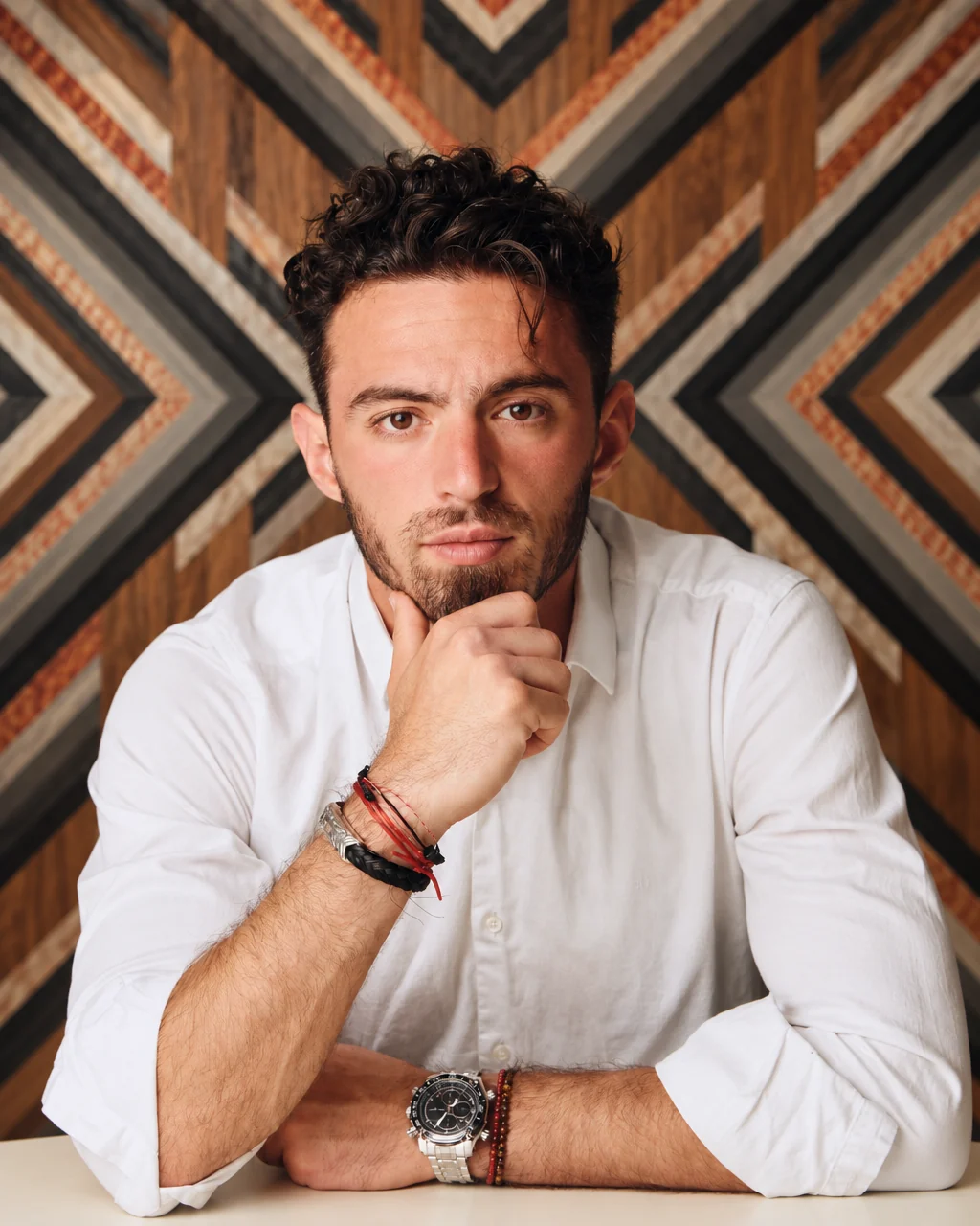 Kodah Pipitone in a white shirt, hand on his chin, in front of a chevron wood wall